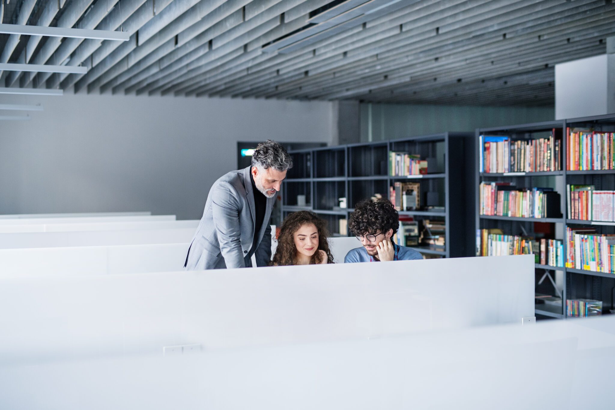 A man helping two children with their studies in a library.