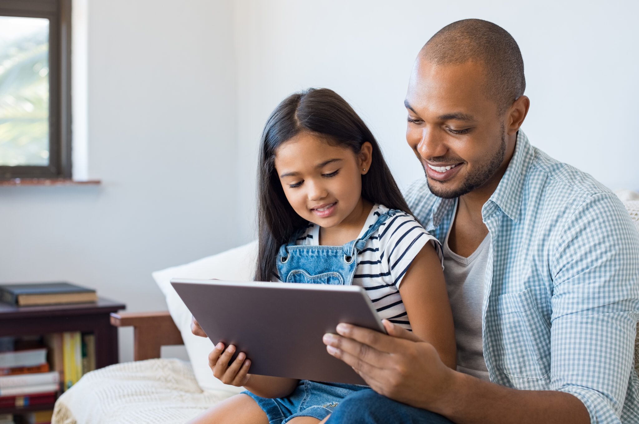 A father and daughter smiling while using a tablet together.