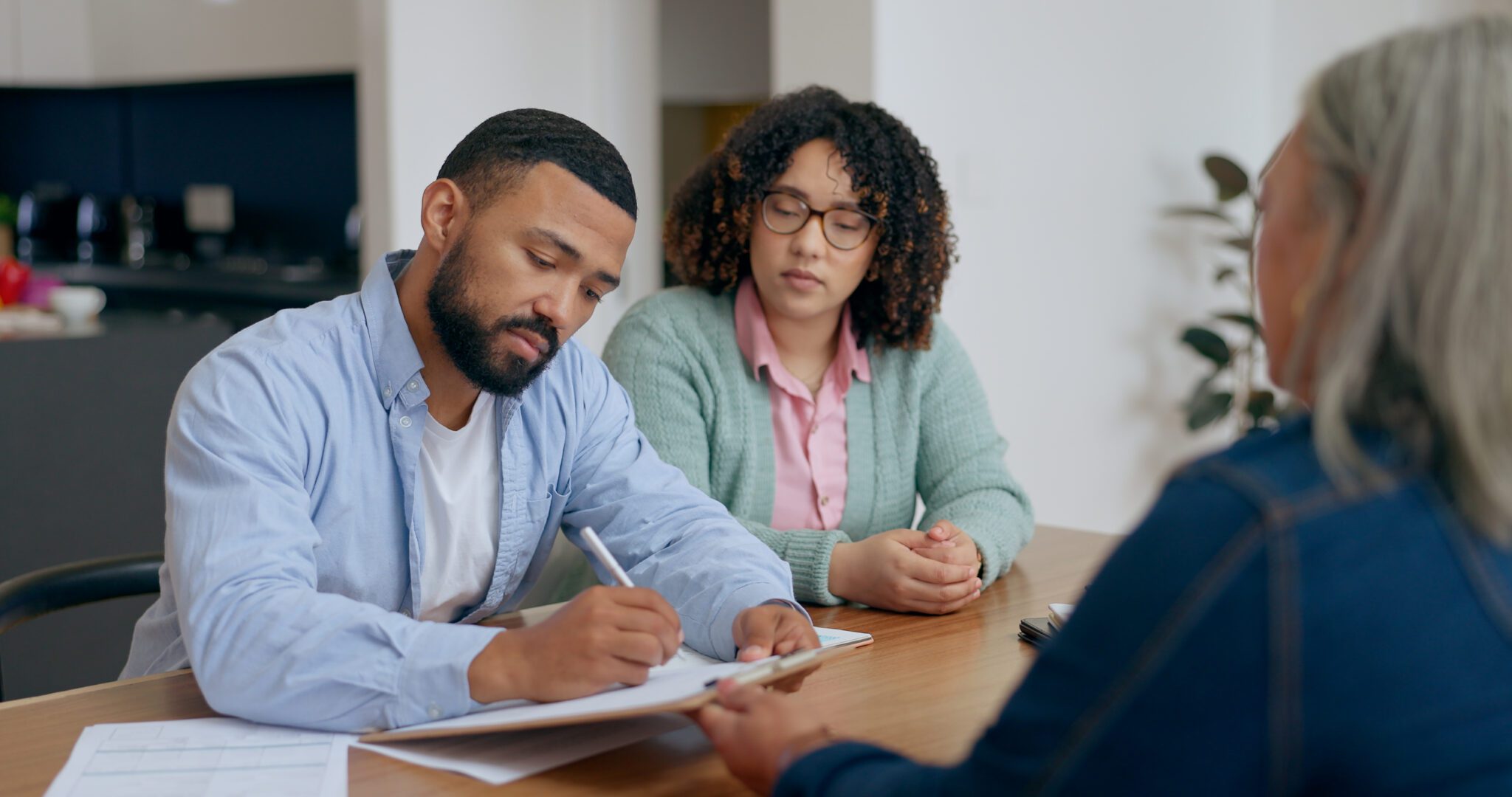 Two people attentively listening to a man while taking notes.
