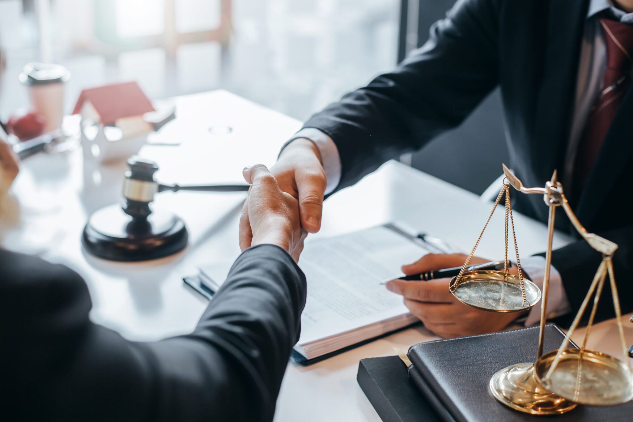 Two people shaking hands over a legal desk with scales and documents.