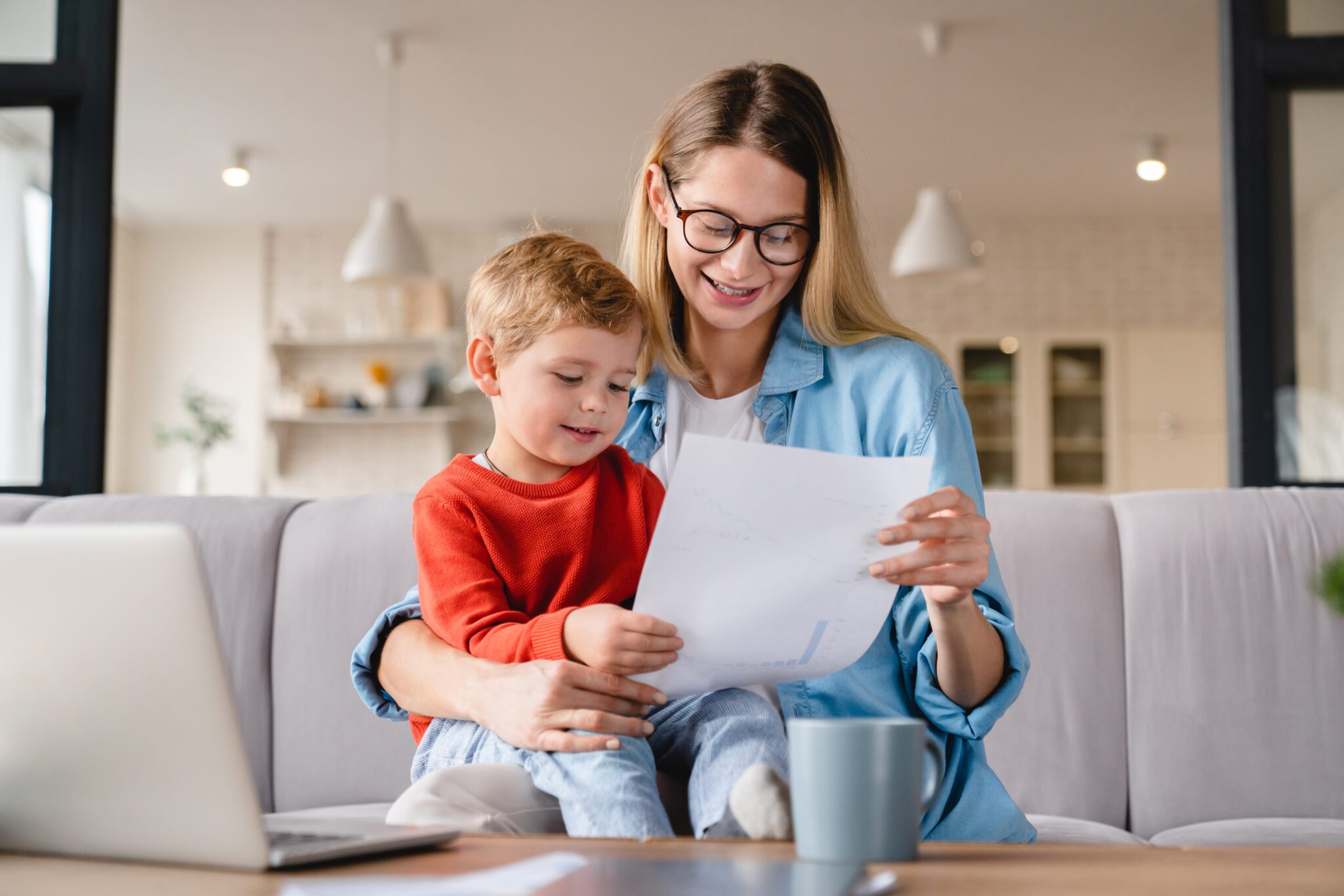 A mother and child reading a paper together on a couch.