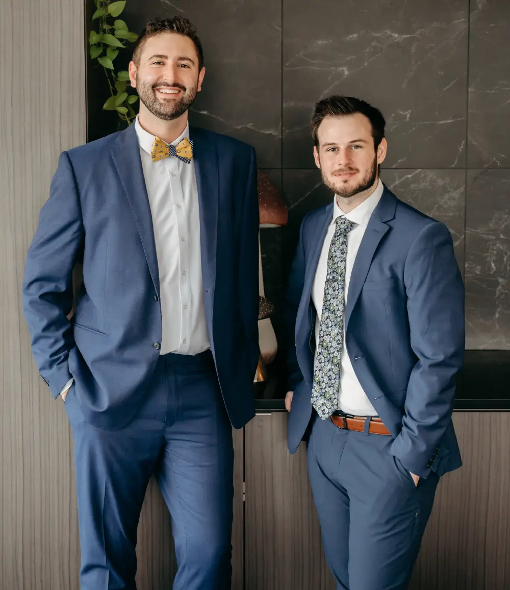 Two men in blue suits standing and smiling indoors.