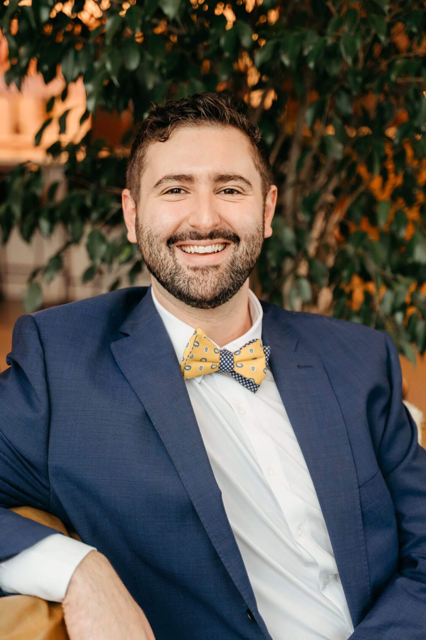 A smiling man in a blue suit and yellow bow tie.
