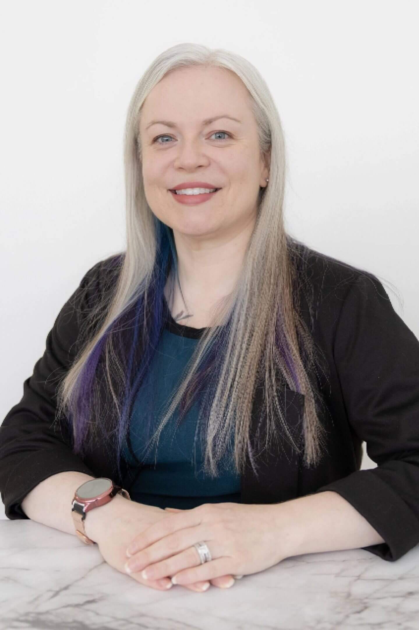 Smiling person with long hair, seated indoors.