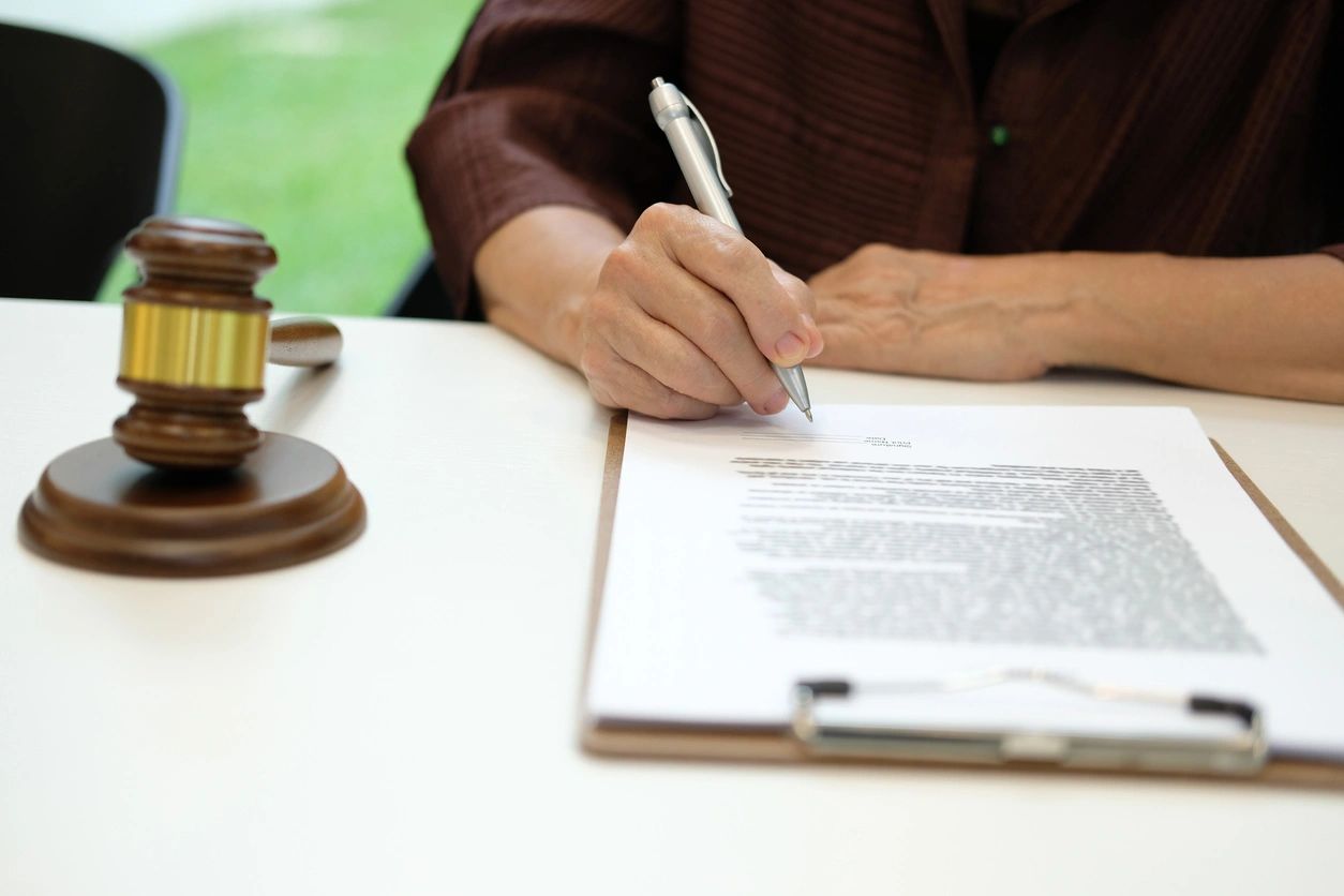 Person signing document beside judge's gavel.