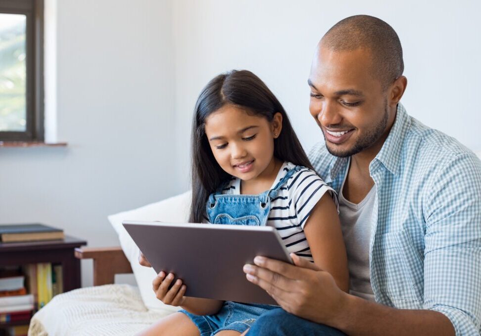 A father and daughter smiling while using a tablet together.