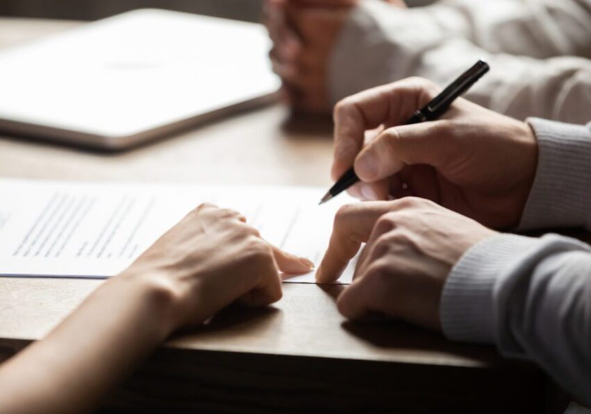 Close-up of hands signing a document on a table.