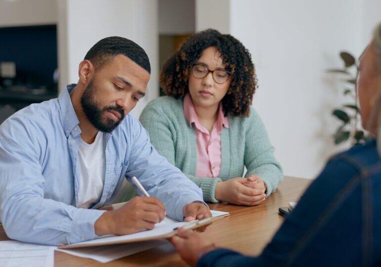Two people attentively listening to a man while taking notes.