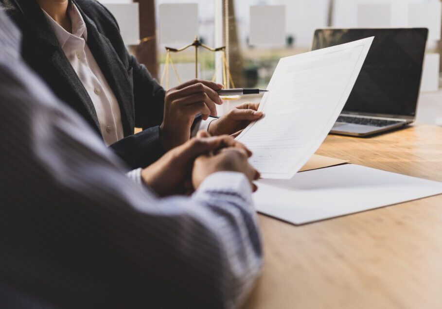 Two people reviewing documents at a desk near a window.