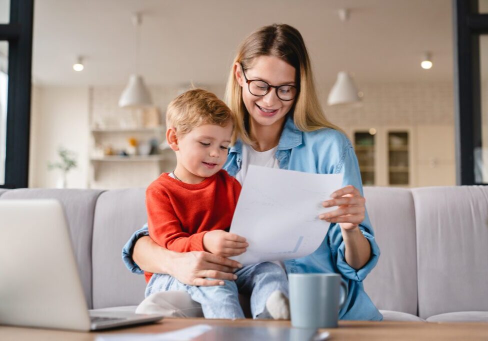 A mother and child reading a paper together on a couch.
