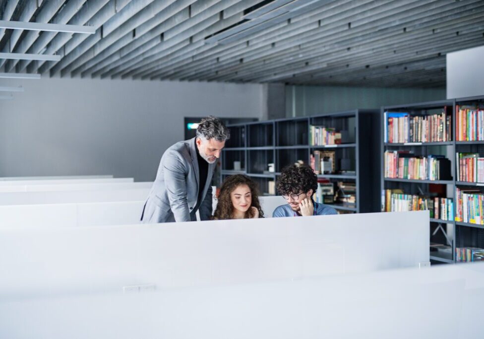 A man helping two children with their studies in a library.
