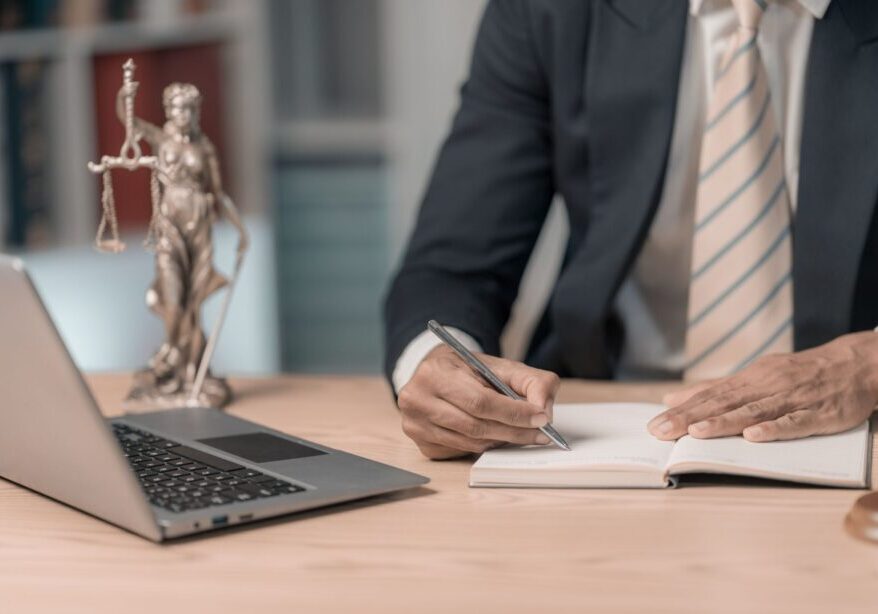 Lawyer writing at desk with laptop.