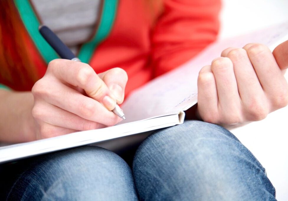 Person writing in notebook on lap.