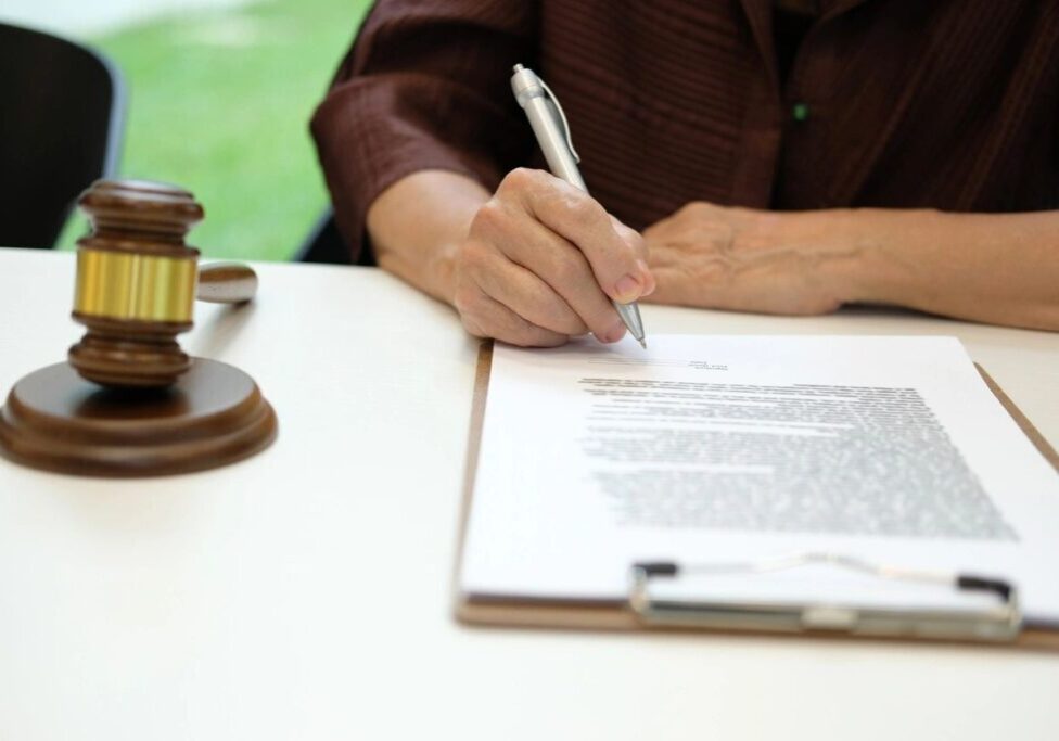 Person signing document beside judge's gavel.